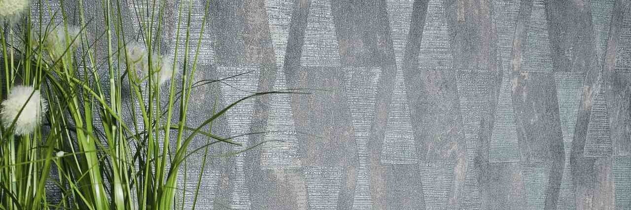 Moderne geometrische Mustertapete in Grau mit strukturierter Oberfläche und vertikalen Formen neben grünen Zimmerpflanzen.